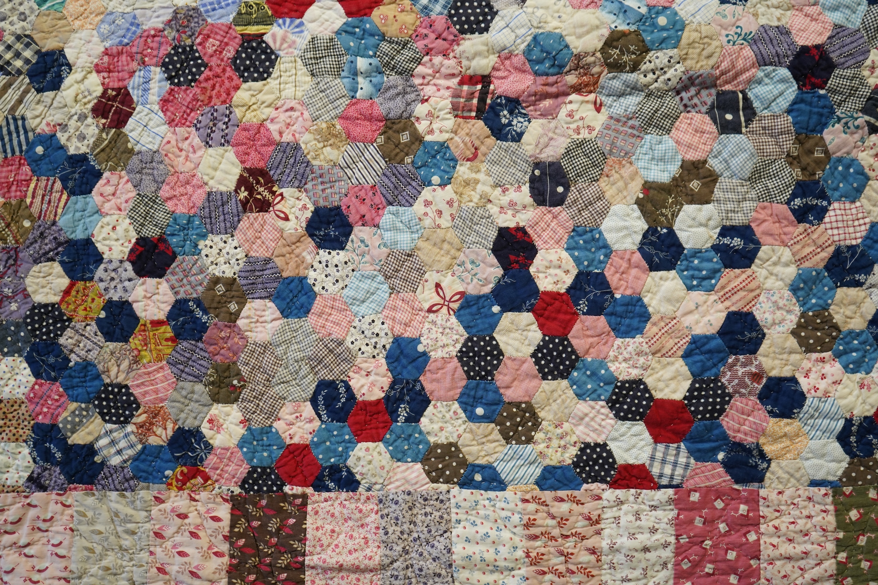 An English cotton hexagon hand made and hand pieced quilt, made from a large variety of printed dress fabrics from 19th century. The quilt edged with a wide stripped multi fabric border. The under side designed in wide s